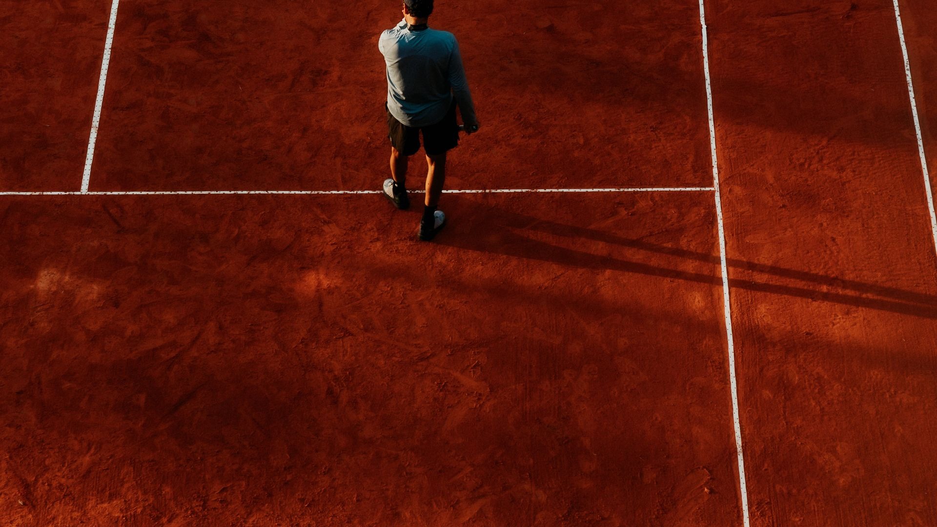 Male tennis player on a red clay court at dusk
