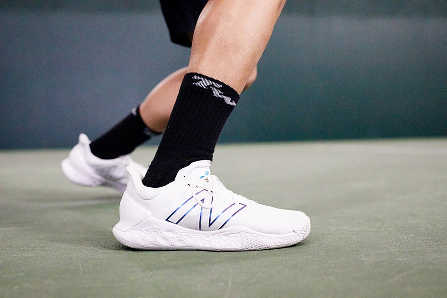 Close-up of a player's feet in New Balance court shoes working at the baseline
