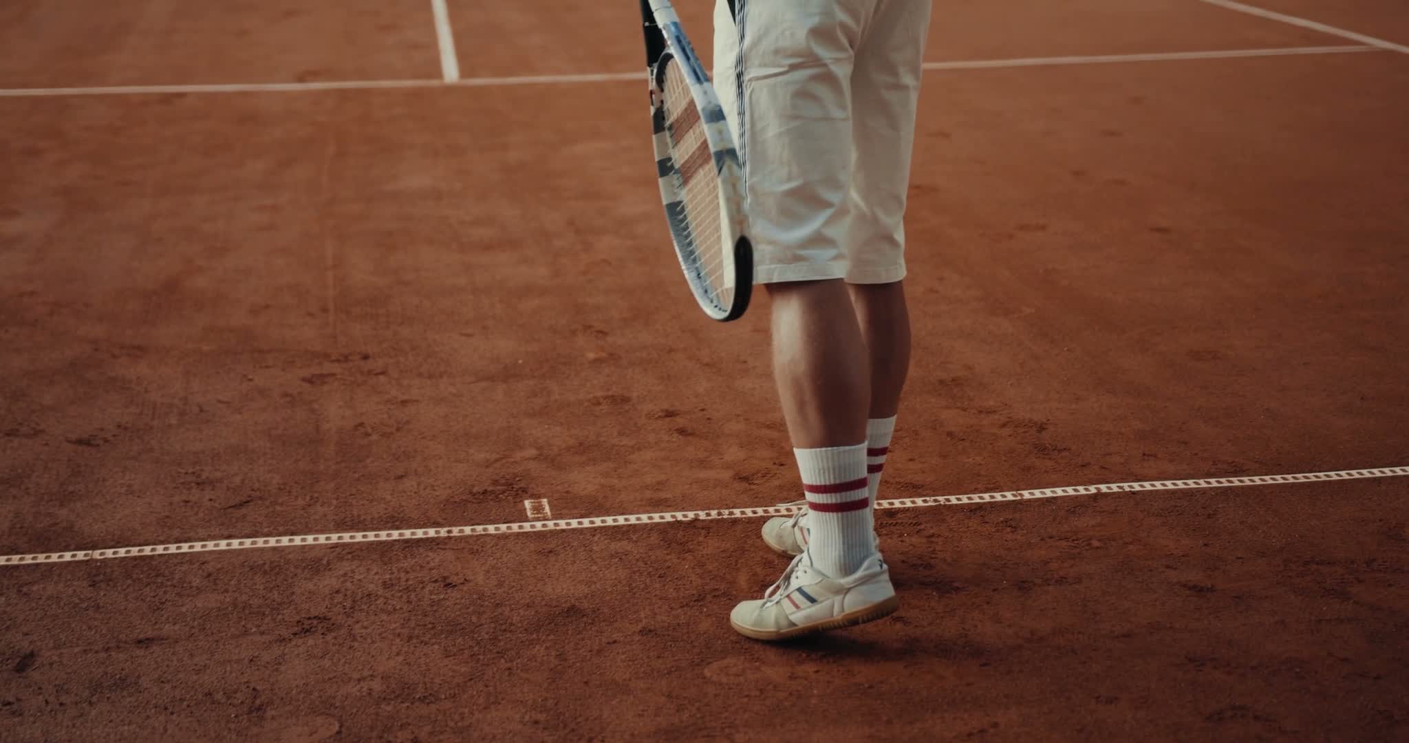 Player's feet planted wide at the baseline in retro court shoes on clay